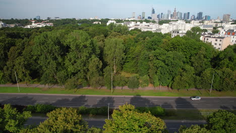 Aerial-lateral-shot-along-highway-with-driving-cars-in-suburb-district-of-Warsaw-City---Modern-Skyline-with-high-rise-buildings-in-background,-Poland