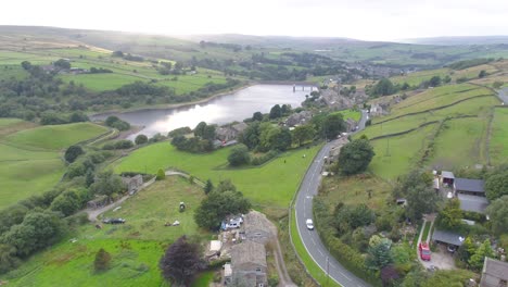 drone footage panning from the bottom of a small yorkshire countryside valley to the top of the hill, including village stone houses, farms, country roads, dry stone walls, reservoir and moors