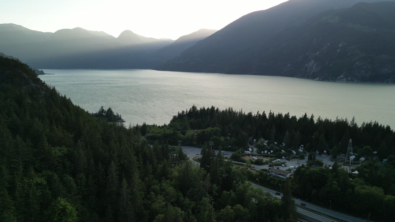 Drone footage of Howe Sound with forested hills and mountains near Squamish, British Columbia, featuring calm blue water and rugged landscape.