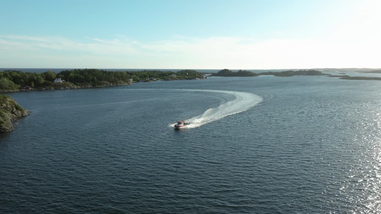 A boat glides across a tranquil sea on a sunny afternoon. The surrounding landscape features islands under a clear blue sky, creating a peaceful coastal scene
