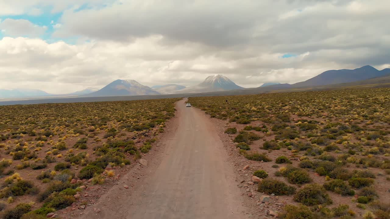toma cinematográfica aérea que distancia un auto solitario en un camino de tierra en el desierto de atacama, chile, sudamérica