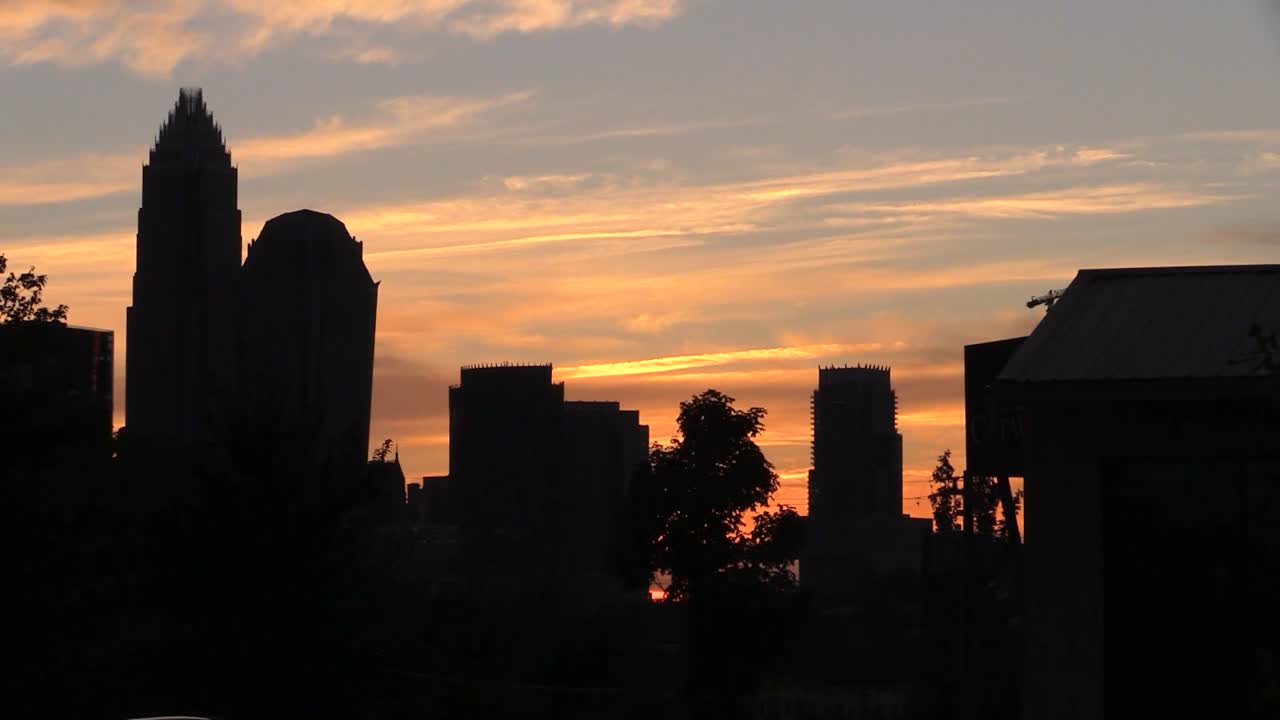 Atardecer cautivador sobre un paisaje urbano con rascacielos en silueta. El cielo está pintado con naranjas y amarillos vibrantes, creando un impresionante panorama urbano. Escena urbana, tranquila y atmosférica.