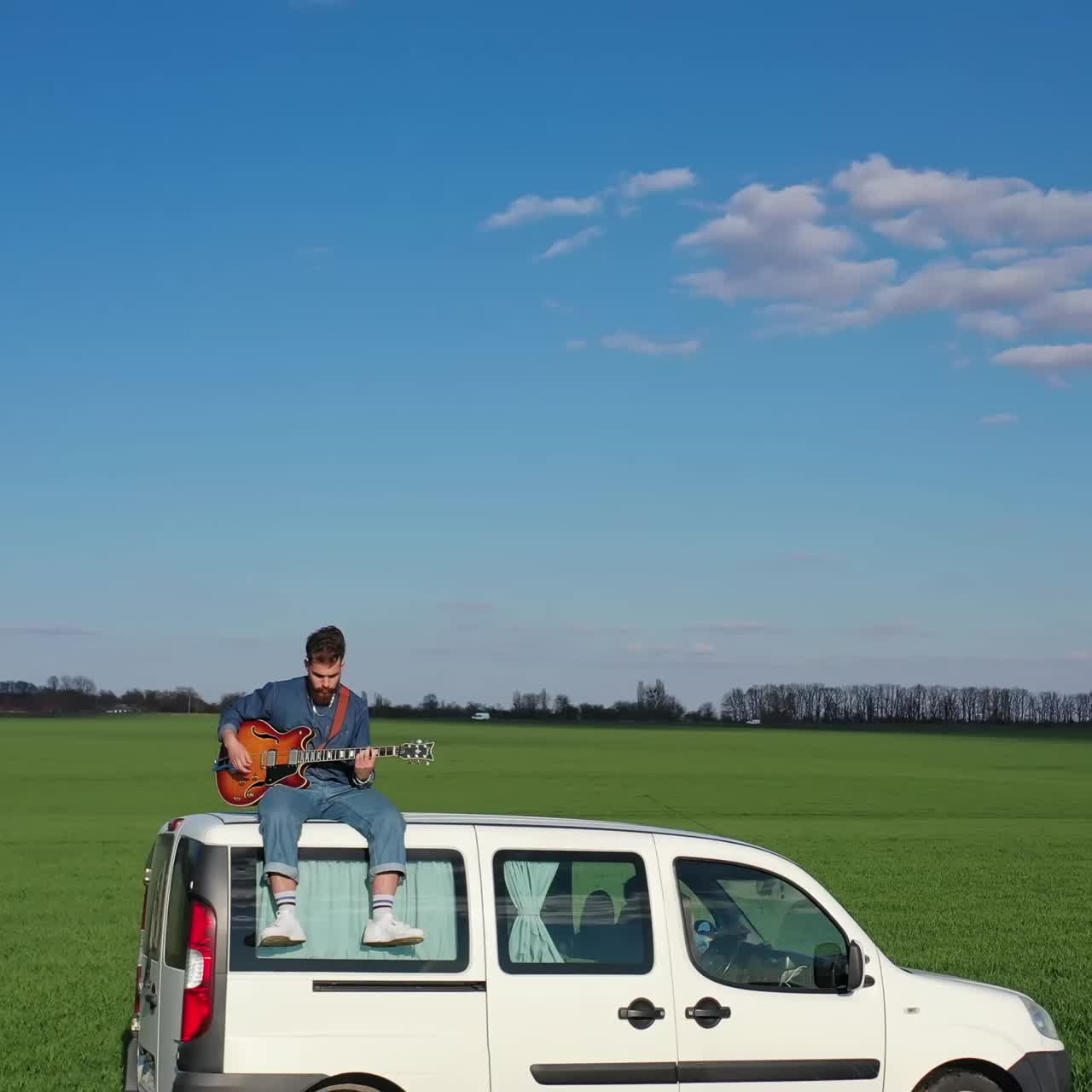 Uomo che suona la chitarra sull'auto. Giovane uomo seduto sull'auto e che suona la chitarra.