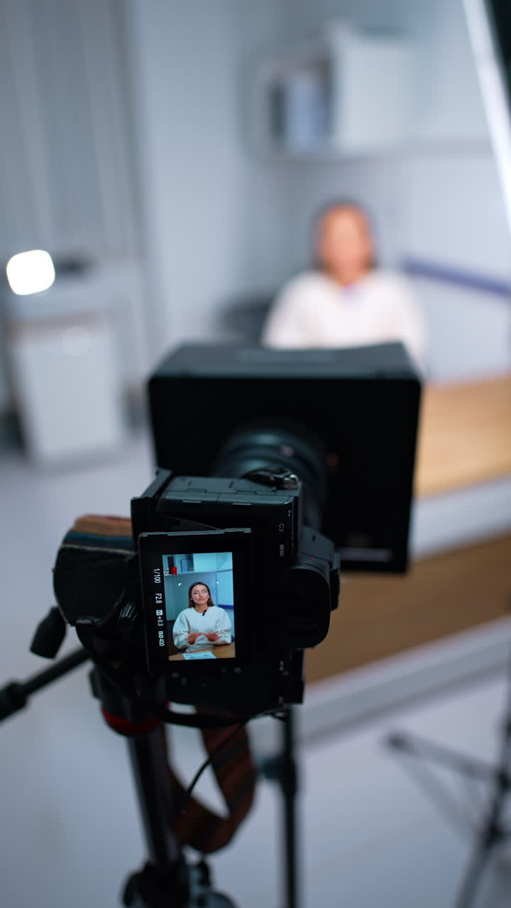 Woman speaking on the display of modern camera on tripod. Blogging concept. Close up. Blurred backdrop. Vertical video.
