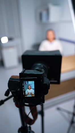 woman speaking on the display of modern camera on tripod. blogging concept. close up. blurred backdrop. vertical video.
