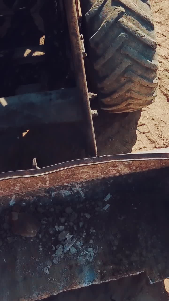 bulldozer with huge wheels and a bucket is moving around the territory of a sandy quarry. Close-up. Vertical video