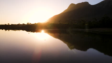 aerial - drone flying horizontally, just above surface of salt pan, golden sunset and mountain silhouette reflected in water