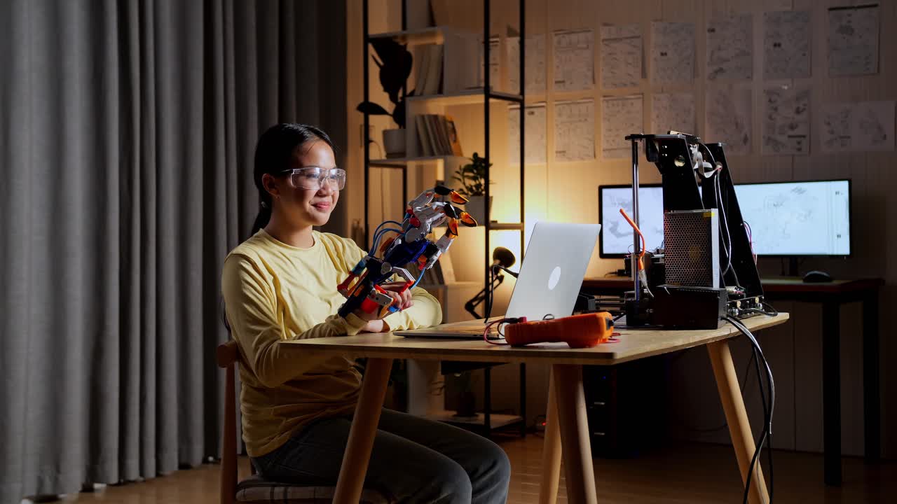 만족스러운 십대 아시아 소녀가 집에서 노트북을 사용하면서 사이보그 손을 보고 확인하고 있습니다.