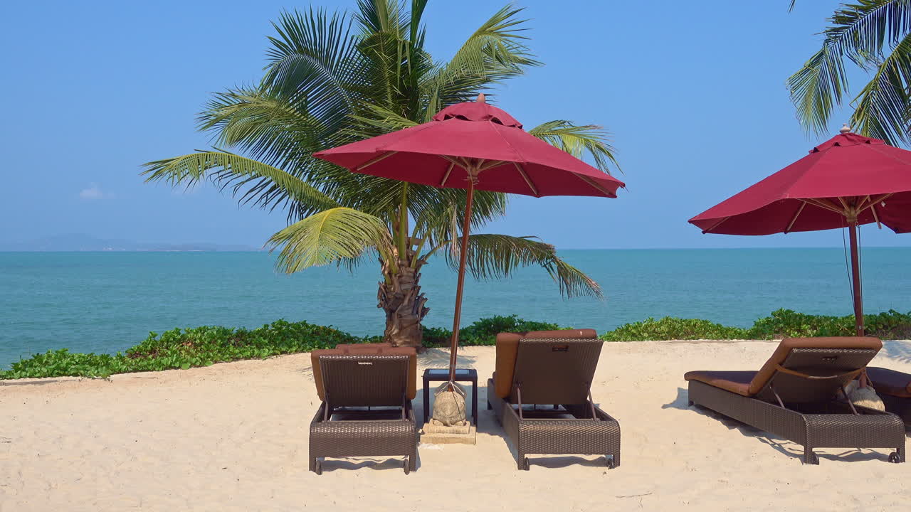Wooden deck chairs under red umbrella on the beach with sea view