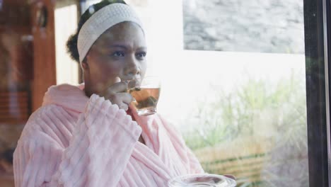 African-american-plus-size-woman-wearing-bathrobe-and-drinking-tea-at-spa,-unaltered,-slow-motion