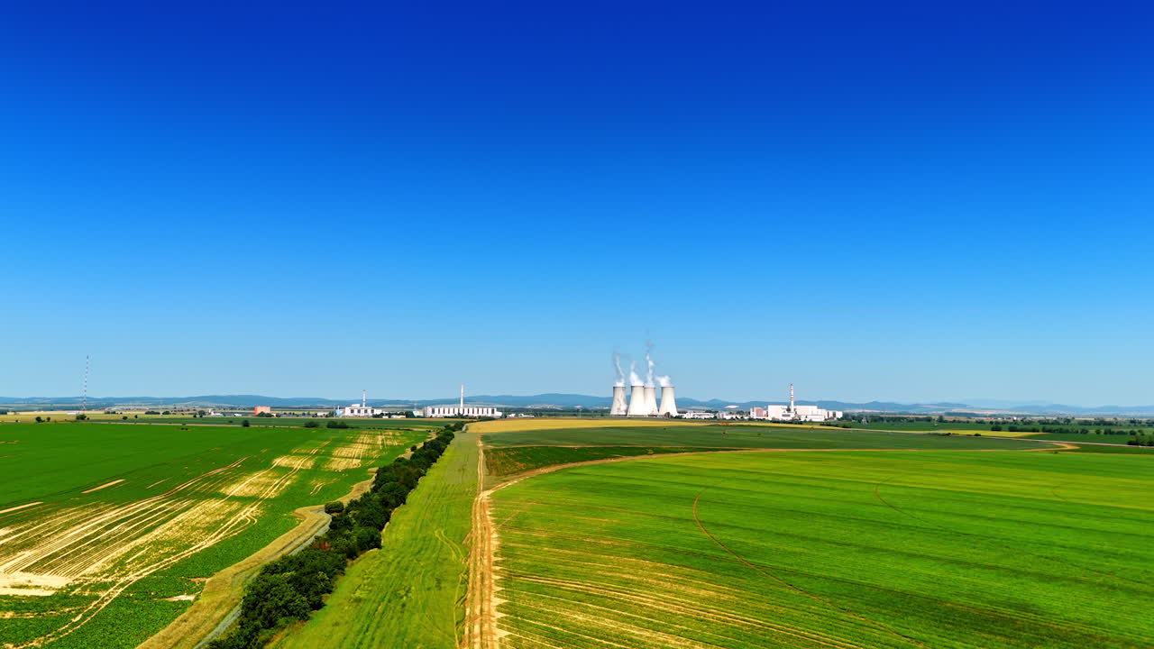 Power plants in clear sky. Green fields extend to power plants under a bright blue sky, highlighting energy production