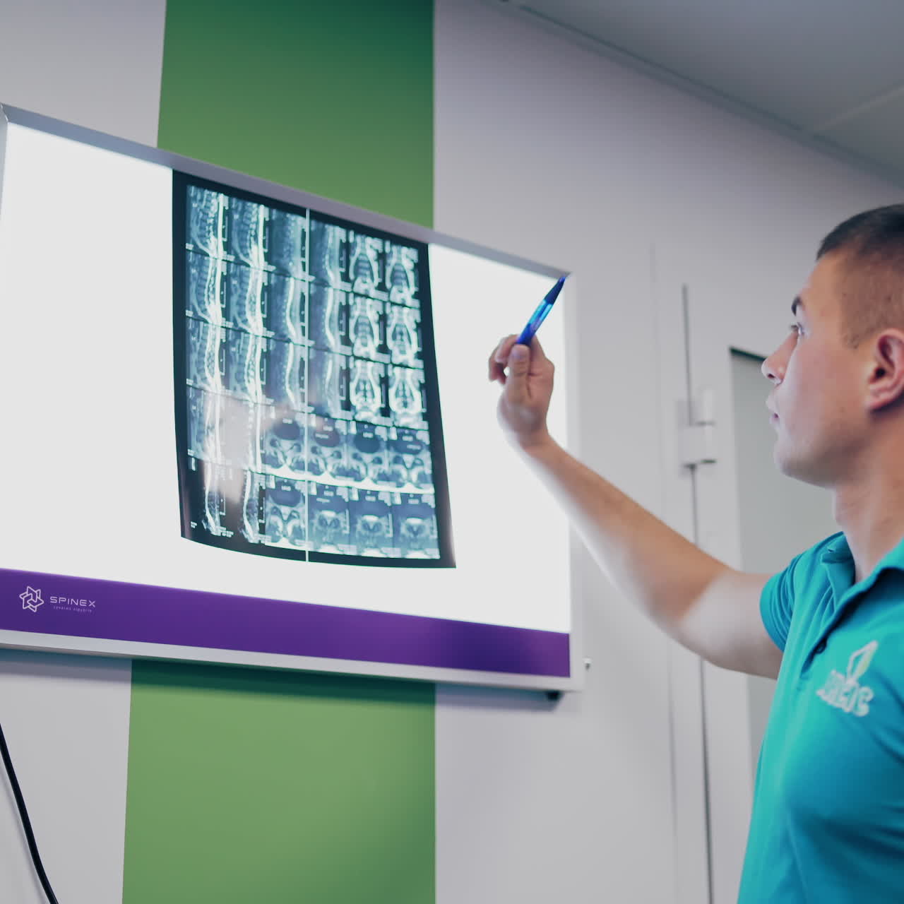 Doctor is talking about the back problem while looking at x-ray on the background of a hospital. X-ray photograph is hanging on a whiteboard and a specialist tells the results of backbone.