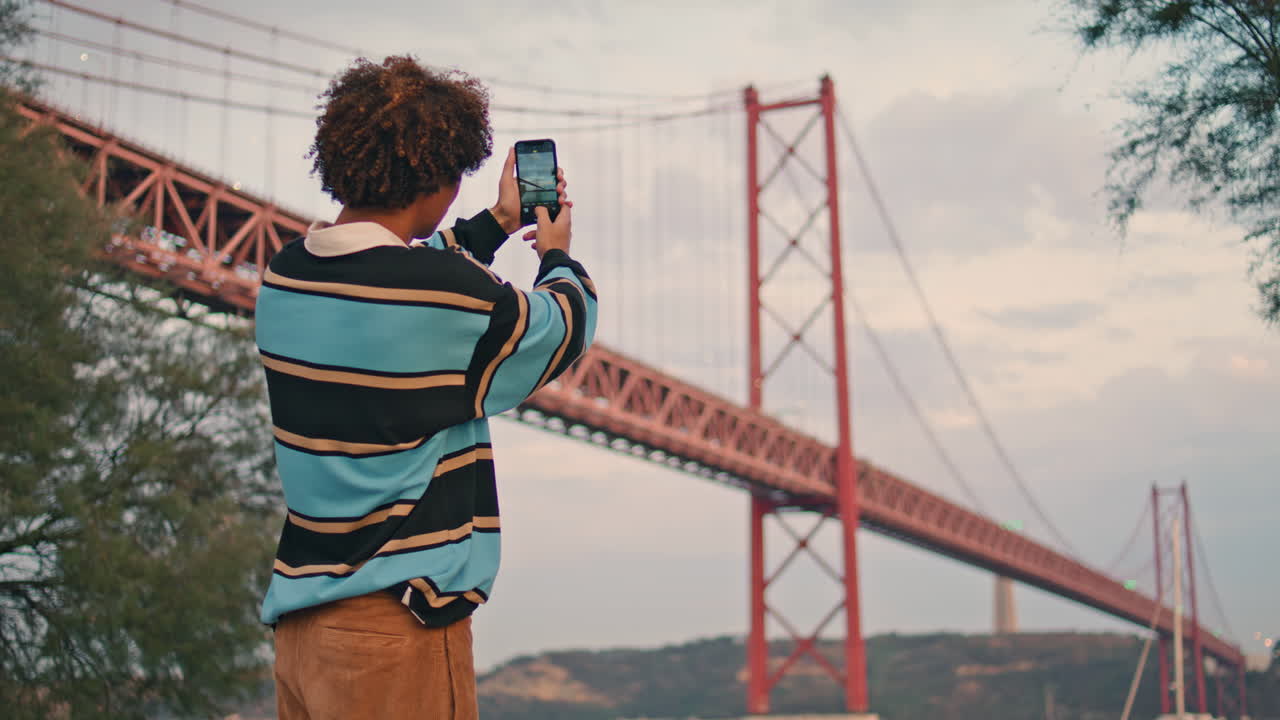 joven turista fotografiando el puente en primer plano por la noche. tipo con teléfono inteligente vertical