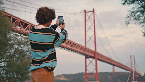 young tourist photographing bridge evening closeup. guy with smartphone vertical