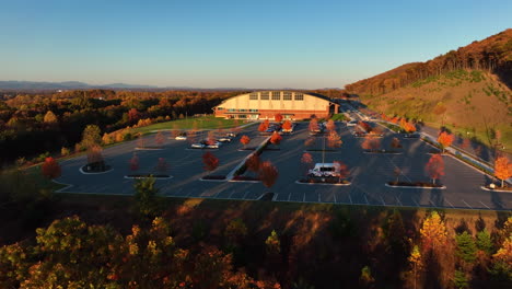 aerial approach of large sports facility building and parking lot on side of mountain during autumn fall foliage