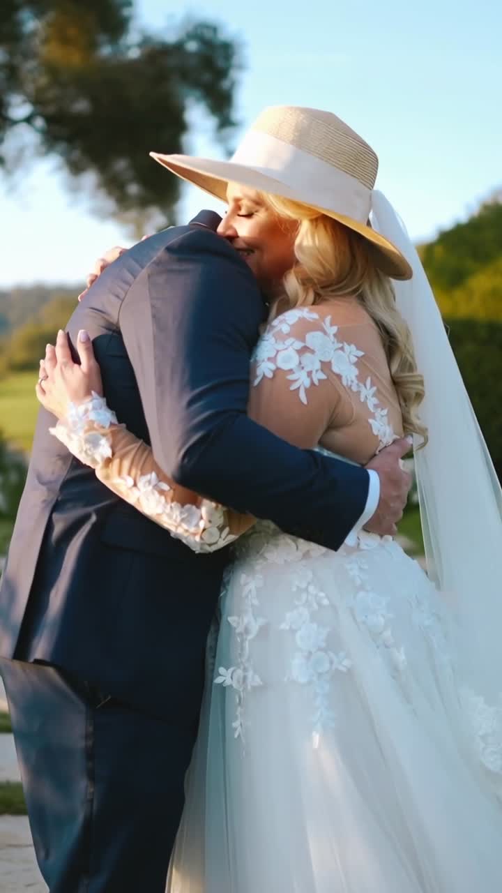 Video verticale: Sposo che si china e abbraccia la sposa su un sentiero di pietra, scambiandosi le promesse, con cappello a tesa larga.