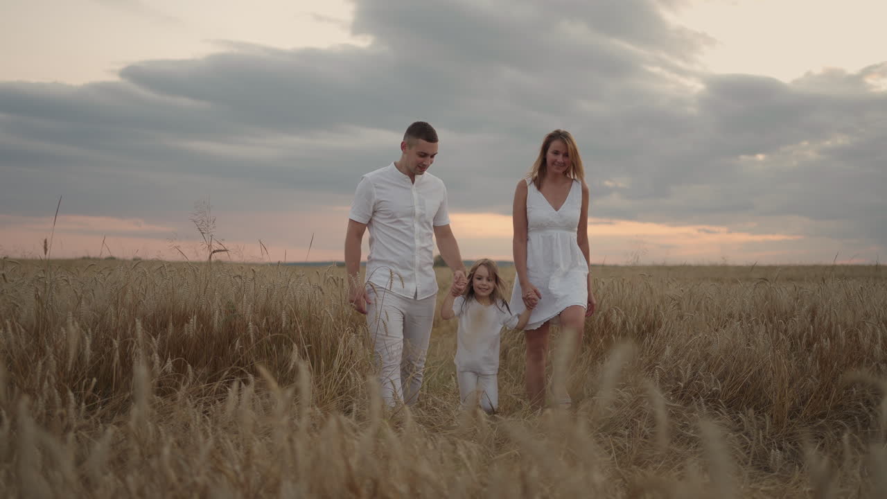 Slow motion: Happy family of farmers with child are walking on wheat field. Healthy mother father and little daughter enjoying nature together outdoors.