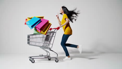 energetic woman running with shopping cart and colorful bags