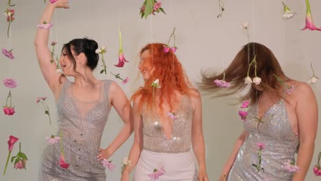 three joyful women are dancing exuberantly beneath a cascade of hanging flowers while wearing three joyful women are dancing exuberantly beneath a cascade of hanging flowers while wearing sparkling dresses