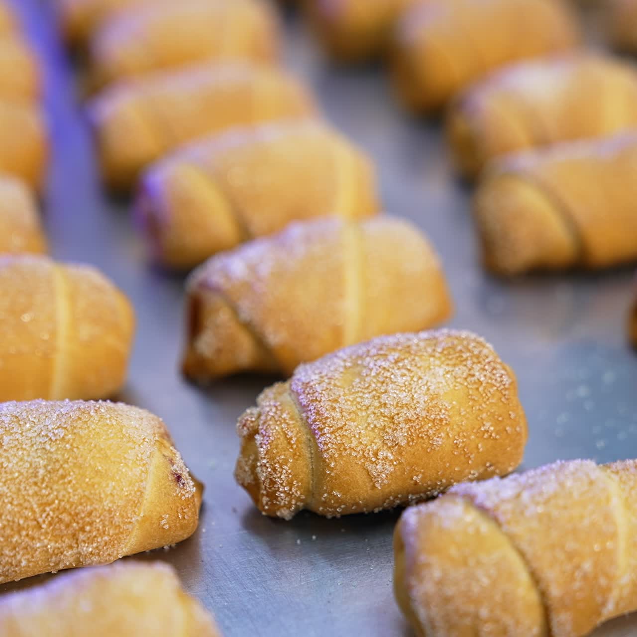 Ready-made croissants coated with sugar on the baking sheet. Little sweet desserts manufactured at bakery. Close up