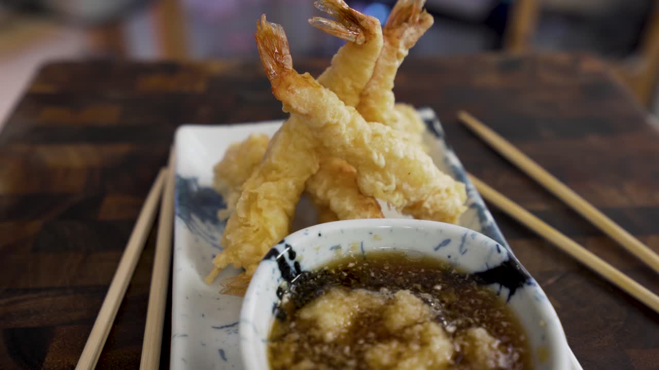 Camarão tempura com molho tradicional para tempura em prato azul e branco e fundo de madeira girando, comida japonesa.