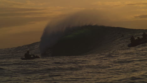 Ocean-spray-flies-off-top-of-wave-crashing-into-barrel-under-orange-haze-sunset