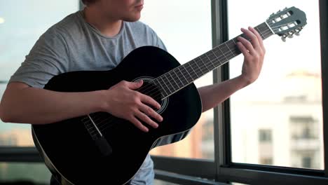 man playing acoustic guitar by the window