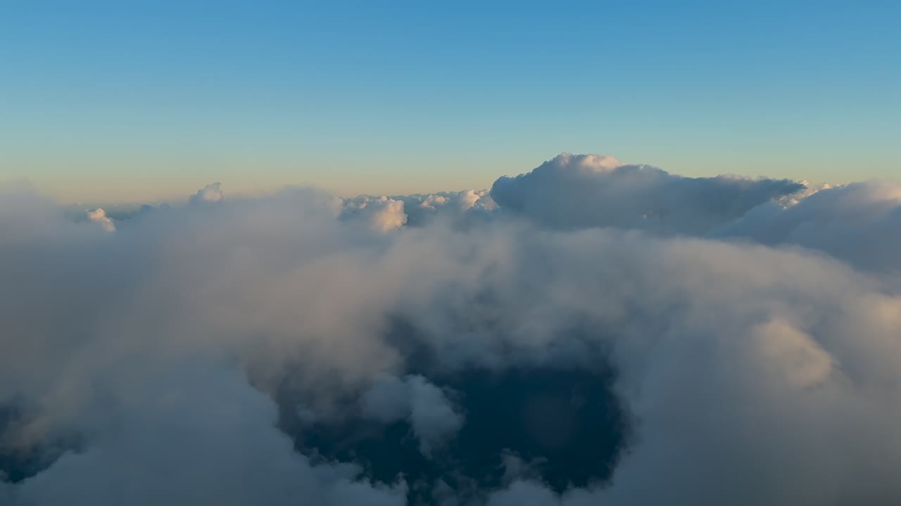 An immersive pilot’s eye view in a peaceful flight over golden clouds illuminated by the sunset light under a soft blue sky