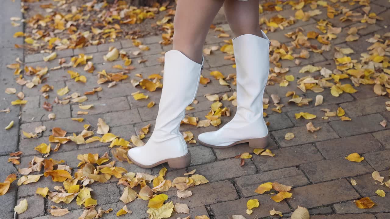 mujer jugoso pateando hojas de otoño en una acera