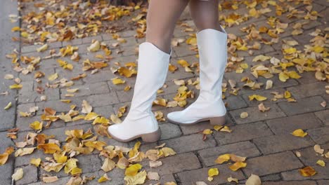 woman playfully kicking autumn leaves on a sidewalk