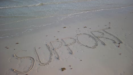 schrägaufnahme einer in den sand geschriebenen unterstützung an einem strand, an dem wasser auf den sand plätschert