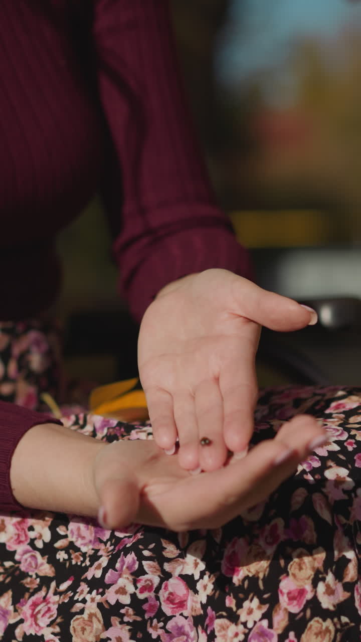 mujer con falda de impresión floral se sienta en silla de ruedas mirando a la mariposa en la palma. insecto rojo vuela lejos de las manos. interacción con la naturaleza en un parque soleado de primer plano