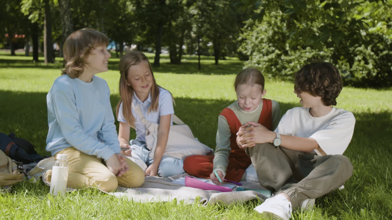 Group of Happy Children Talking and Laughing Together on a Picnic Blanket in a Sunny Park
