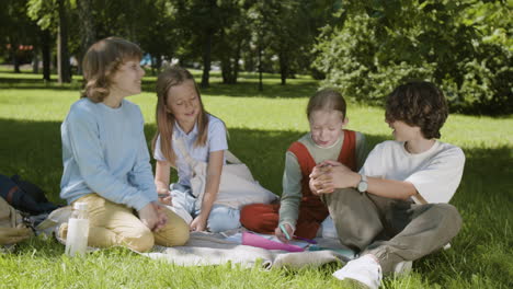 group of happy children talking and laughing together on a picnic blanket in a sunny park
