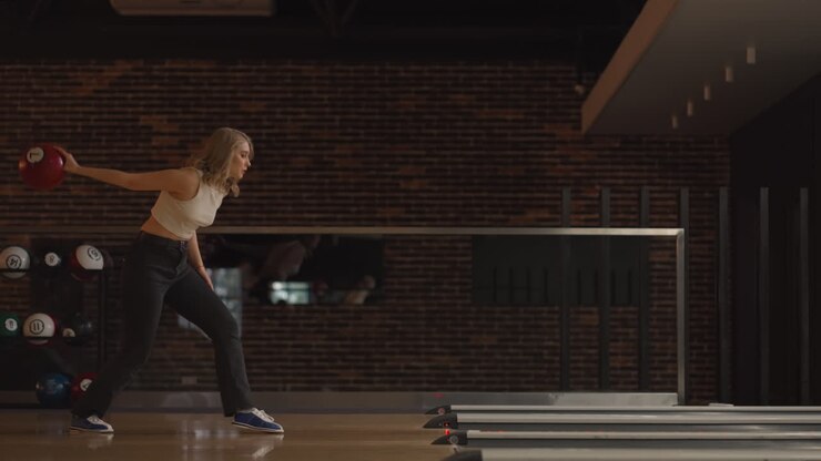 Ensom kaukasisk blond kvinde kaster en bowlingkugle og slår en strike med ét kast, danser, jubler og springer af glæde.