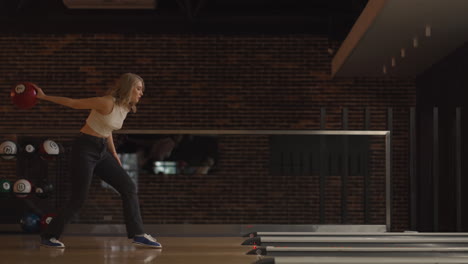 alone caucasian blonde woman throws a bowling ball and knocks out a shoot with one throw dances rejoices and jumps with happiness