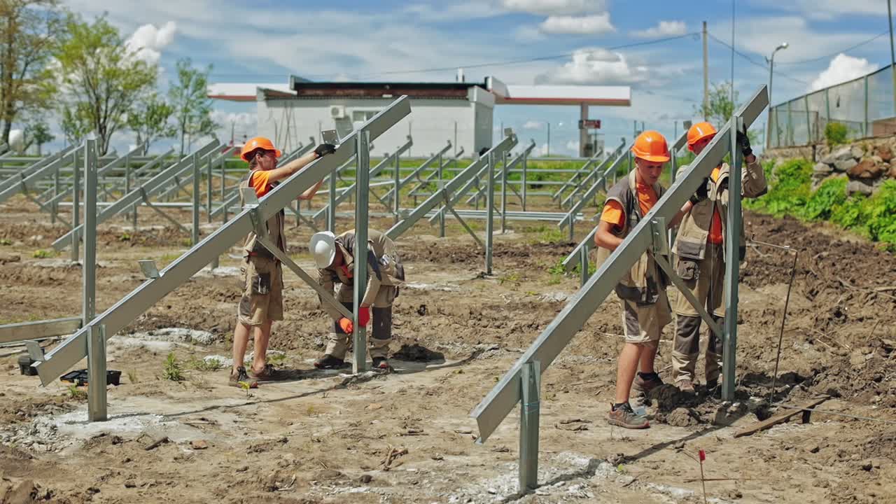 Metal construction for solar panels. Workers in protective helmets build new solar farm on the field in summer.