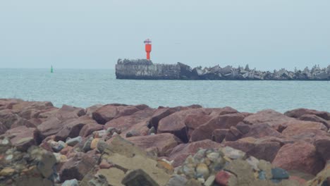 Vista-Distante-En-ángulo-Bajo-Del-Muelle-De-Piedra-Cerca-Del-Puerto-De-Liepaja-,-Día-De-Otoño-Nublado,-Baliza-De-Navegación-Del-Puerto-Rojo,-Mar-En-Calma