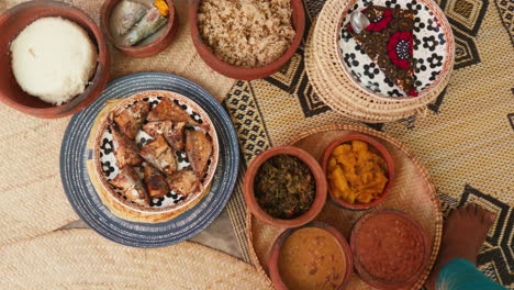 description: the image depicts an overhead view of a variety of dishes laid out on a woven mat, suggesting a traditional african meal setting