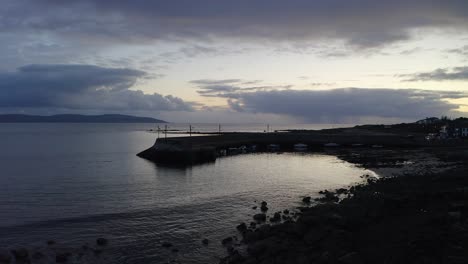 drone pullback from barna pier galway ireland at dusk as light reflects on ocean