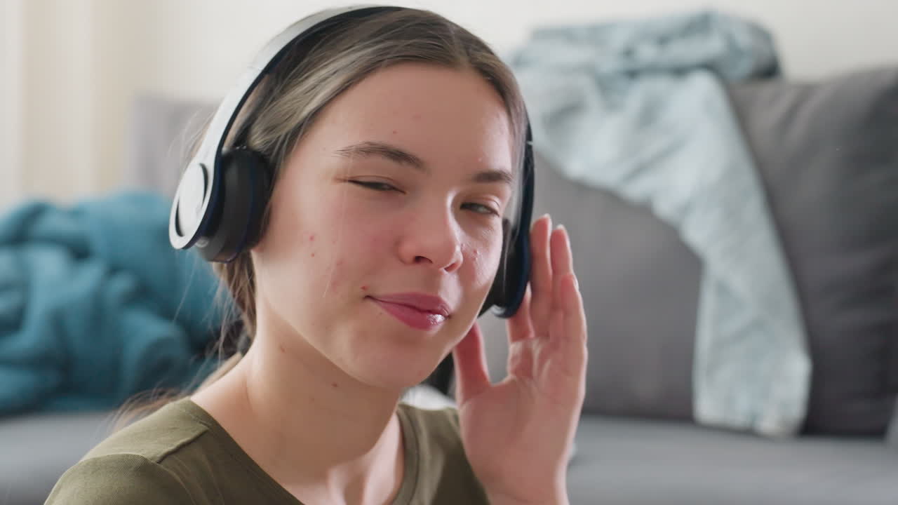 Lady with headphones adjusting earpiece while smiling warmly, enjoying pleasant sound and music indoors, soft natural light highlighting face with serene joyful expression