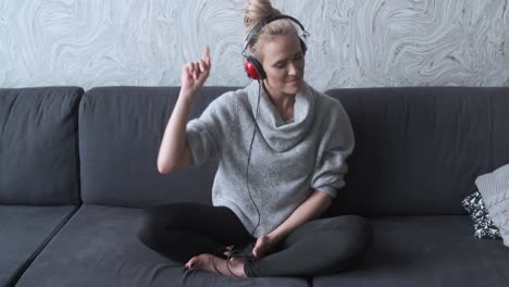 adorable middle aged blond woman sitting on sofa in her home and listen to the music