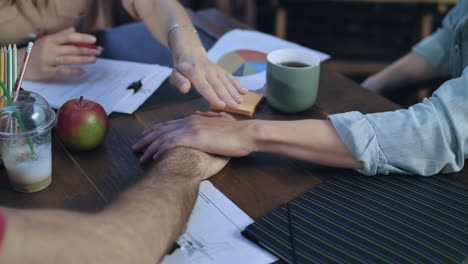 business people putting their hands on each other on table