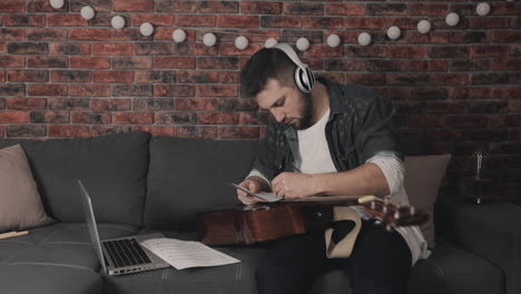 young musician man creating music for guitar, having ideas, taking notes at home