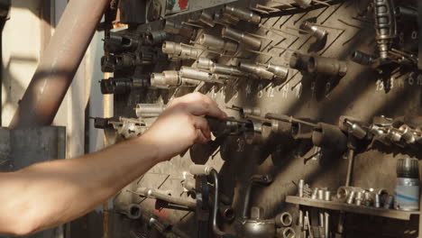 Mechanic's-hand-picks-up-a-tool-hanging-on-a-wooden-board-in-a-car-workshop