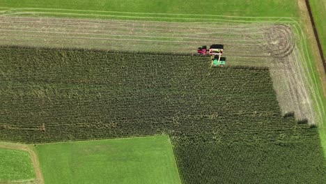 a tractor harvesting corn in a field on a bright day in switzerland, aerial view