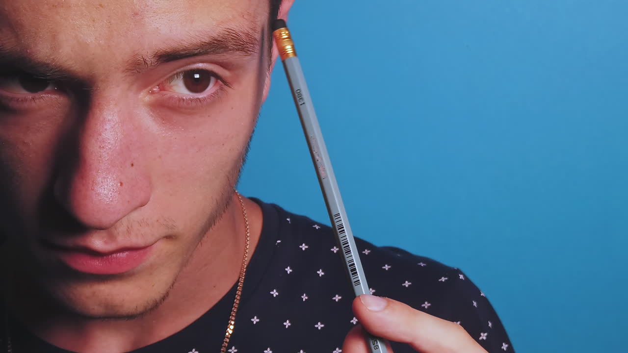 Close-up slow motion of thinking man with a pencil in front of a blue background