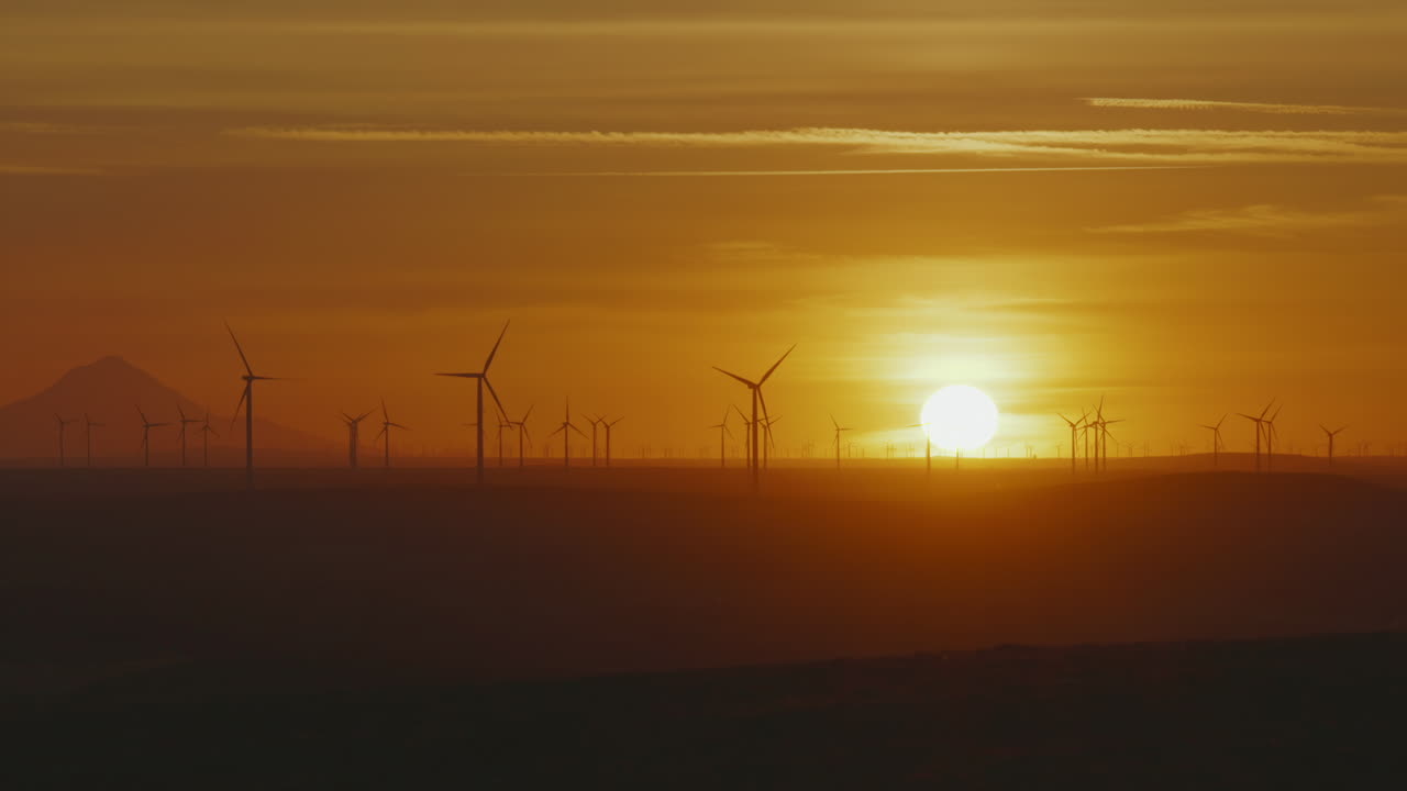 Silhouette Of Wind Turbines Spinning Near Mount Hood In Oregon With Sunlit Background. wide zoom-out