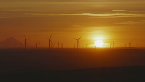 silhouette of wind turbines spinning near mount hood in oregon with sunlit background. wide zoom-out