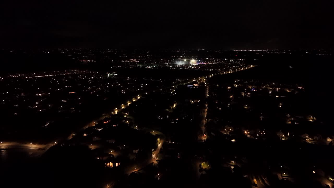Peaceful night scene with lighting lantern in American town. Aerial wide shot. Illuminated stadium in background. Houses along streets of United States on cold winter night. Serene atmosphere